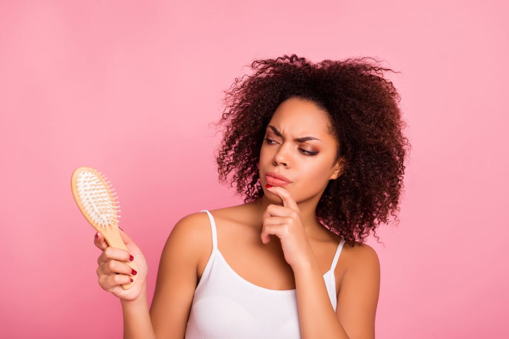 Una mujer mira un cepillo mientras considera hacerse un trasplante de pelo.