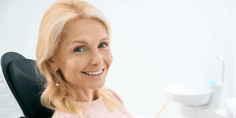 Ältere Frau mit weißem Haar sitzt lächelnd im Zahnarztstuhl