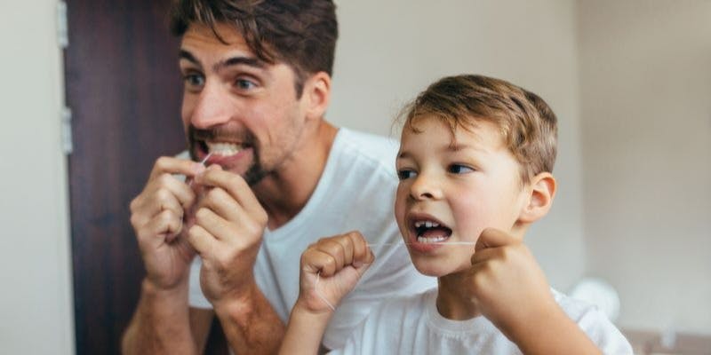 Dad and son flossing: a preventative measure against getting a black tooth.