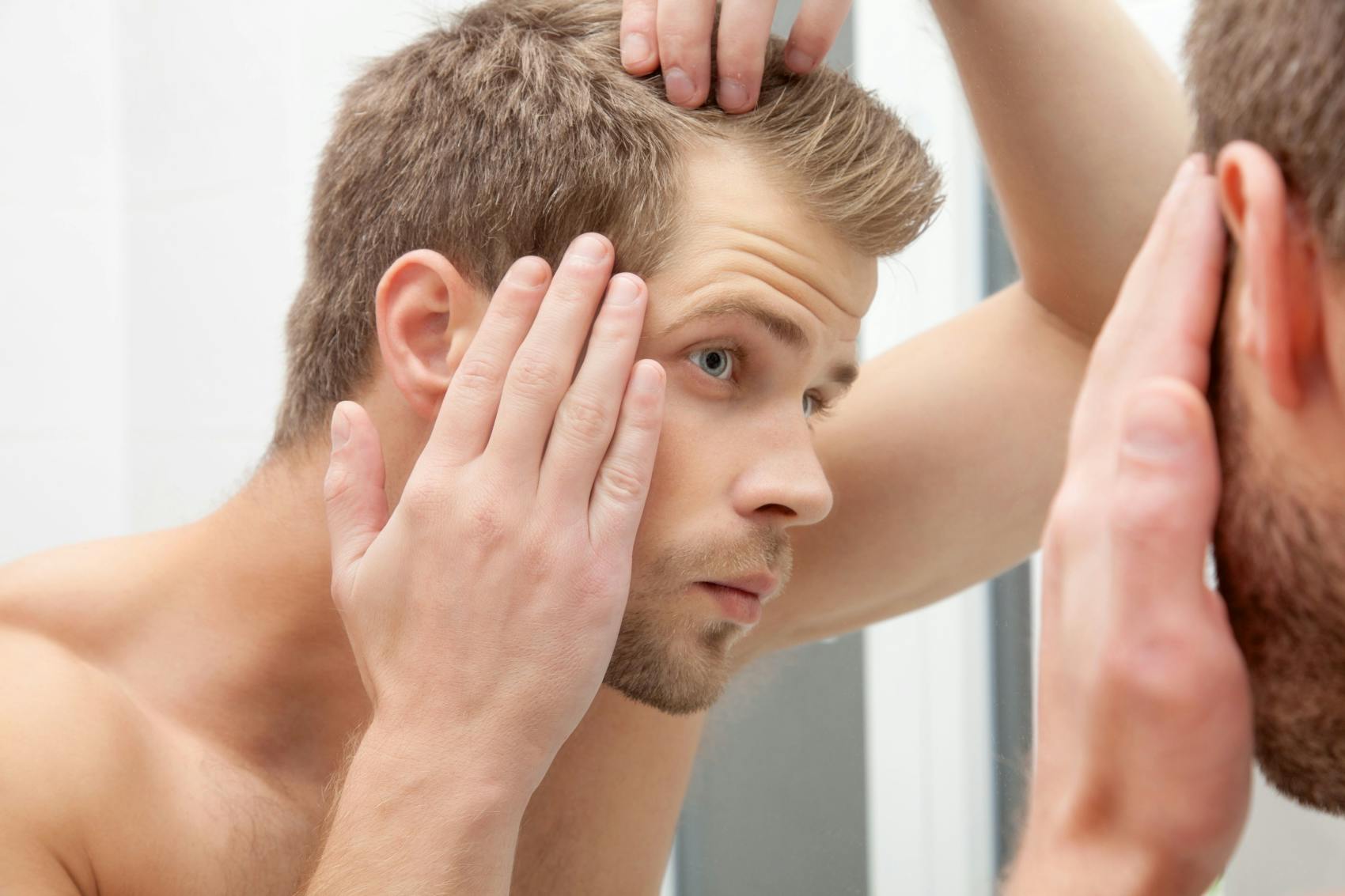Man looking in a mirror at his hairline 